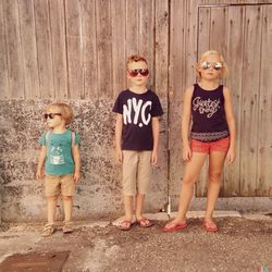 Portrait of siblings standing against wooden fence