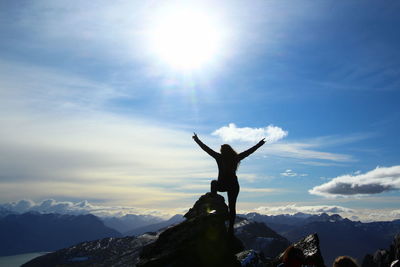 Silhouette woman standing with arms raised on mountain peak