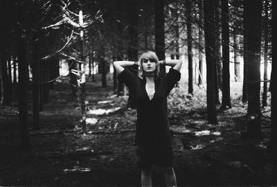 Portrait of beautiful woman with hands behind head standing in forest