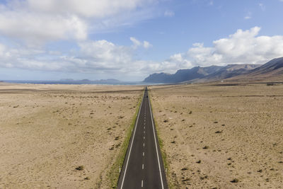 Aerial view of a person walking along the straight road crossing a desert valley in lanzarote