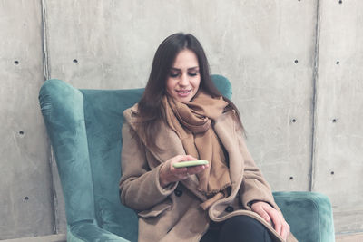 Full length of young woman using mobile phone while sitting outdoors