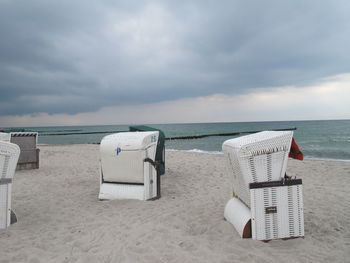 Hooded chairs on beach against cloudy sky