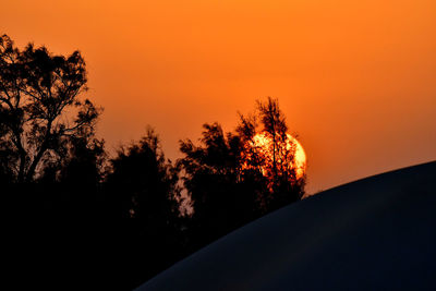 Silhouette trees against orange sky