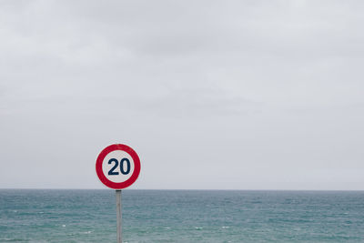 Warning sign by sea against sky