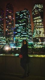 Woman standing against illuminated cityscape at night