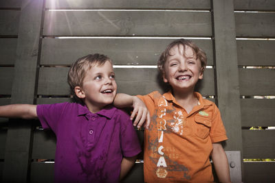 Two cheerful brothers standing against wooden fence