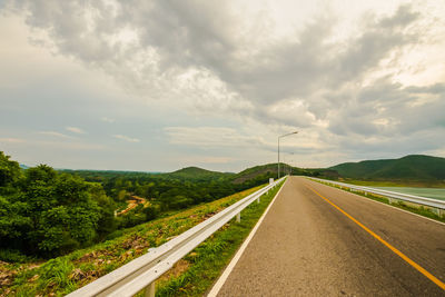 Empty road along plants and trees against sky