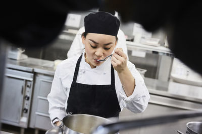 Female chef tasting food from cooking pan at commercial kitchen