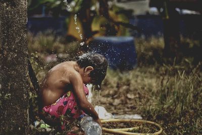 Shirtless girl crouching under falling water in village