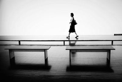 Full length of woman walking on footpath by benches during monsoon