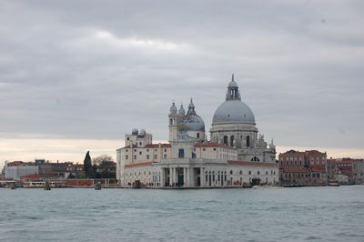 View of buildings at waterfront against cloudy sky