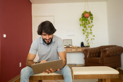  man working at home from his couch with laptop on his lap. man sitting down.  notebook for working.