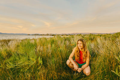 Young woman sitting in tall grass by mono lake in northern california.