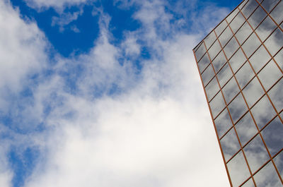 Modern building with a mirror wall reflecting clouds against a blue sky.