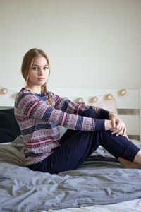 Portrait of young woman sitting on bed at home