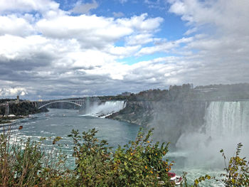 Scenic view of waterfall against cloudy sky