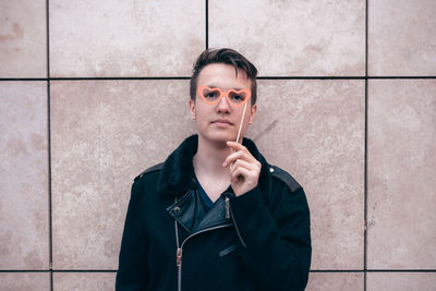 Portrait of young man holding prop standing against wall