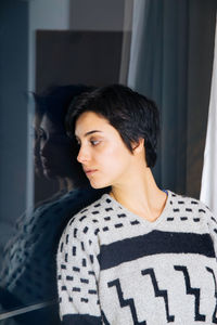 Thoughtful young woman looking through window at home