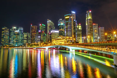 Illuminated bridge over river by buildings against sky at night