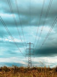 Electricity pylon on field against moody sky