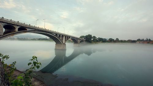 Arch bridge over river against cloudy sky during sunset