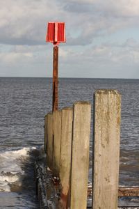 Wooden post by sea against sky