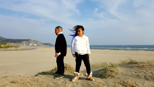 Boy and girl standing at beach against sky