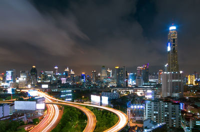 Illuminated street amidst buildings against sky at night