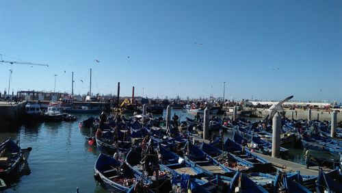 Boats moored at harbor against clear blue sky