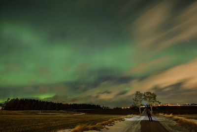 Rear view of man looking at northern lights while standing on road at night