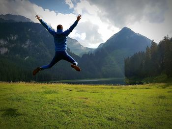 Rear view of man jumping on field against sky