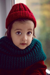 Boy child in red knitted sweater and hat sitting on the window in autumn