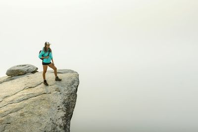 Woman standing on rock by sea against clear sky