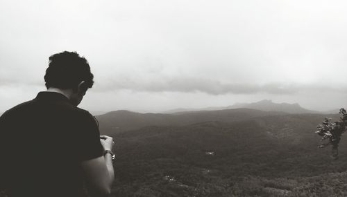 Rear view of man standing on mountain against sky