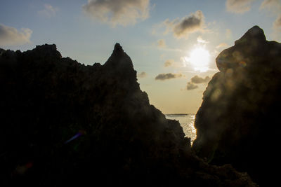 Silhouette rocks by sea against sky during sunset