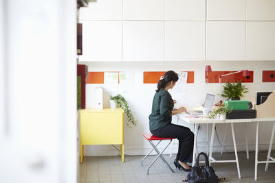 Full length side view of businesswoman with document and laptop at table in office