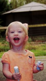 Portrait of cute baby girl holding chalks while standing on footpath