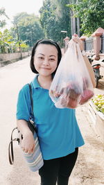 Portrait of young woman showing groceries in plastic bag