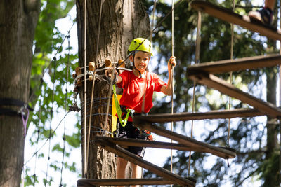 Adventure climbing high wire park - little boy on course in mountain helmet and safety equipment