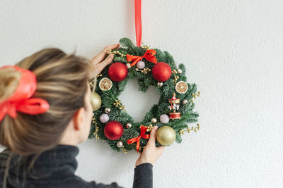 Woman hangs a coniferous wreath on the wall above the sofa, preparing for christmas at home.