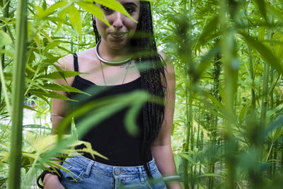 Portrait of smiling young woman standing amidst cannabis plants