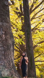 Woman standing by tree trunk in forest