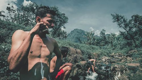 Full length of shirtless man standing against trees