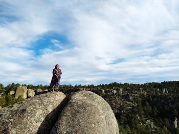 Low angle view of woman standing on rock against sky