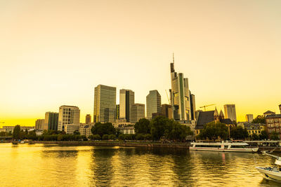 Buildings by river against sky during sunset