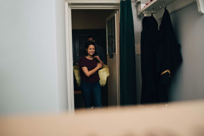 Portrait of smiling woman standing against door at home