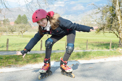 Full length portrait of smiling girl inline skating on road