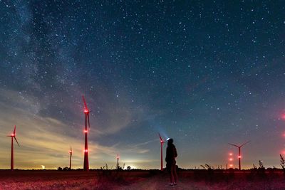 Rear view of man looking at illuminated windmills against star field