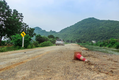 Car on dirt road by land against sky