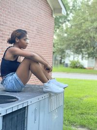 Side view of woman sitting on grass against building